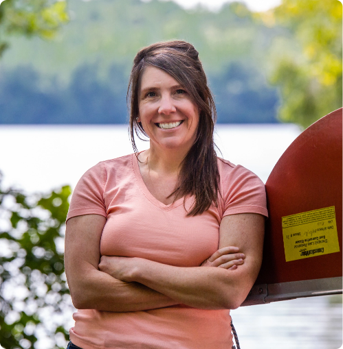 smiling woman leaning against a upside down canoe 