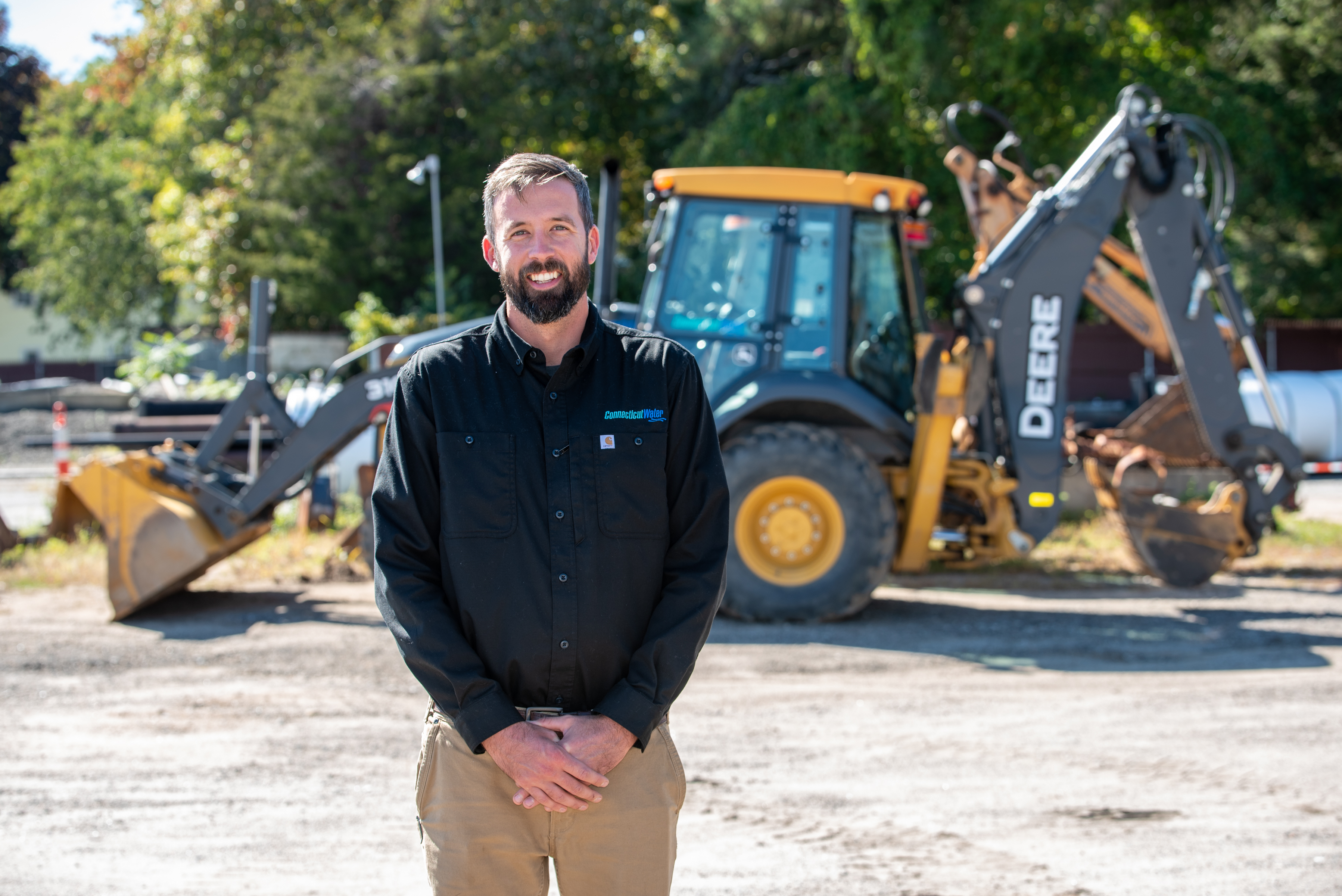 CT Water employee in front of a backhoe looking at the camera and smiling