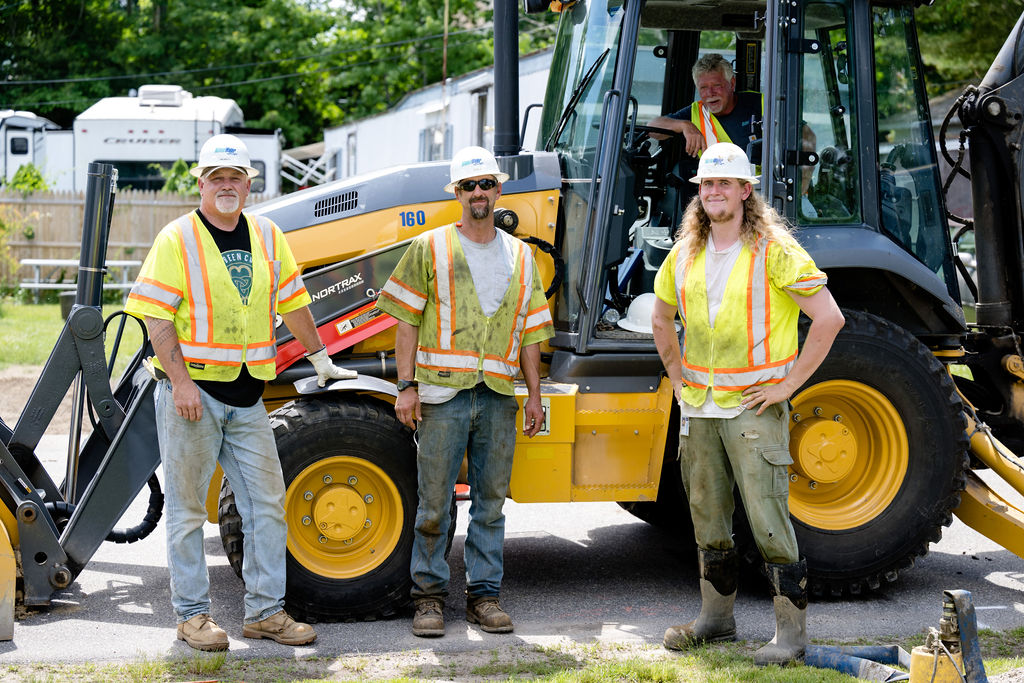 Maine Water employees standing in front of a backhoe vehicle